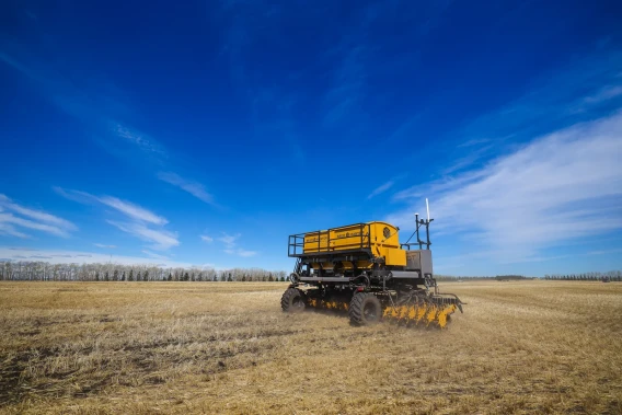 Autonomous seeding machine moving across a harvested field under a clear blue sky.