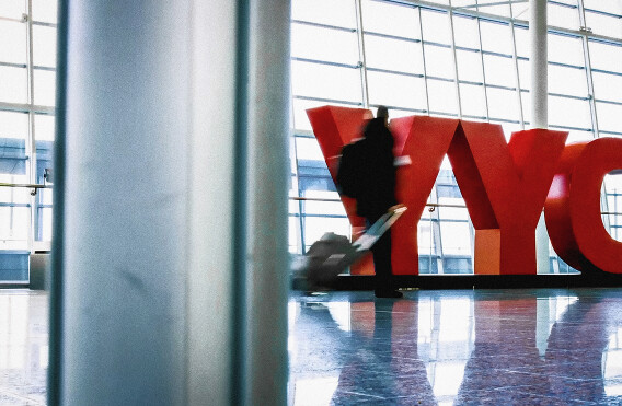 Traveler walking past large red YYC letters in airport terminal.