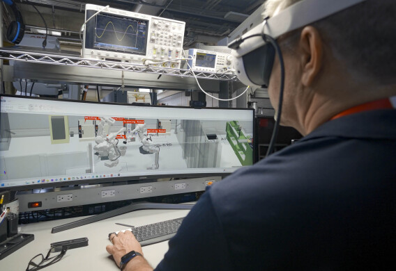An engineer wearing an augmented reality headset works at a computer displaying robotic systems.