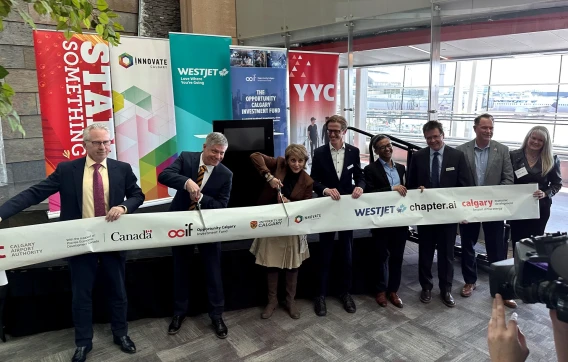 Officials at a ribbon-cutting ceremony inside an airport with YYC and partner banners in the background.