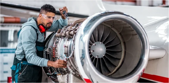 Aviation technician inspecting and servicing a jet engine with tools and protective equipment.