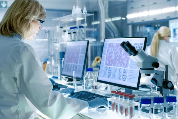 Scientist in a laboratory reviewing research data beside a microscope and sample tubes.