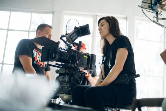 Cinematographer seated beside a professional cinema camera while working on an indoor production set.