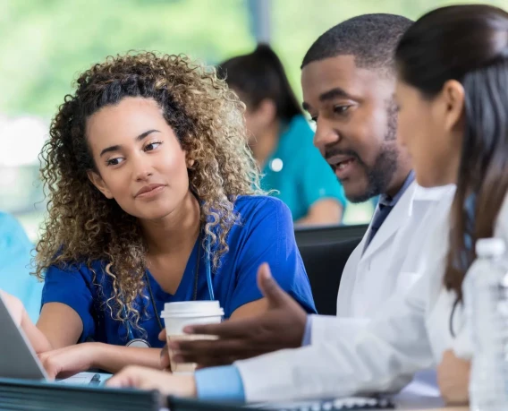 Healthcare professionals in scrubs and a white coat collaborating together around a laptop.