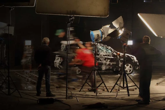 Production crew on a commercial film set lighting a car inside a dark studio.
