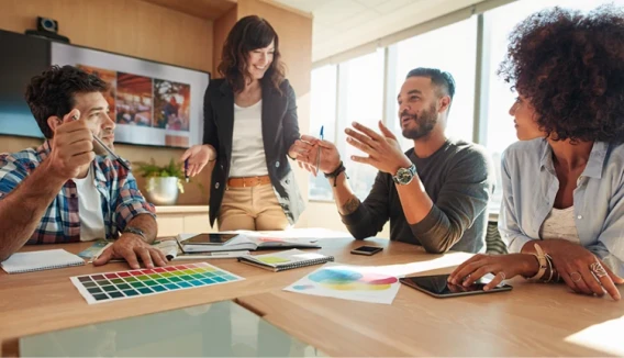 Creative team members discussing ideas around a table during a collaborative office meeting.