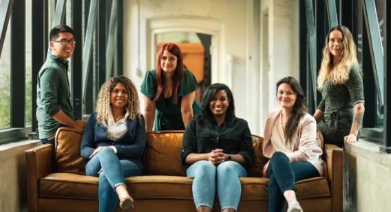 Diverse team portrait of five colleagues posing together on and around a couch in an office lounge.