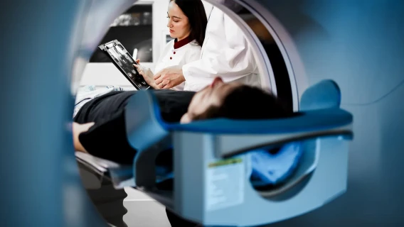 Doctor reviewing scan images while a patient lies inside an MRI machine.