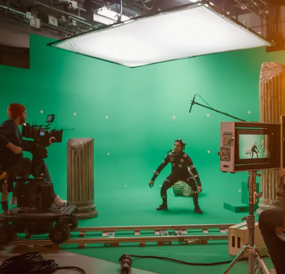 Film production set with green screen backdrop, motion capture performer, camera rig, and studio lighting.