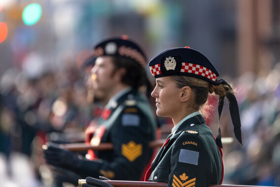 Soldiers in green Canadian dress uniforms and red-and-white berets march with rifles at a Remembrance Day ceremony in Memorial Park Calgary.