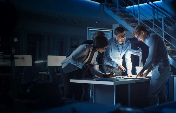 Team members working together late at night around a table in a modern office.