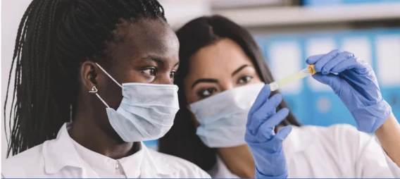 Two masked laboratory scientists closely examining a test sample in a pipette.