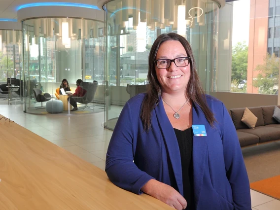 Professional woman standing in a modern office lobby with glass meeting rooms in the background.