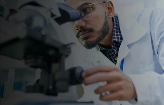 Close-up of a scientist in a lab coat focusing a microscope for laboratory analysis.