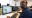 Designer working on CAD building plans across dual monitors in office with printed blueprints