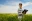 Woman standing in a green field holding a tablet under a bright sky.