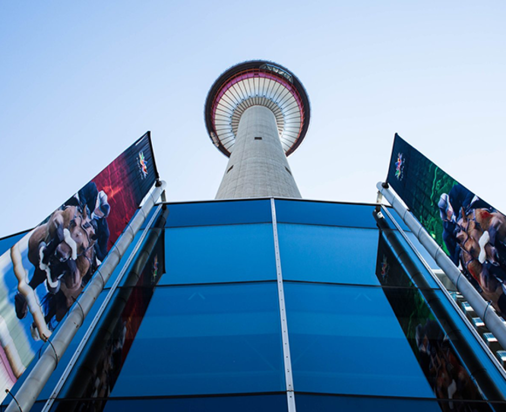 Low-angle view of Calgary Tower with banners and reflective glass panels.