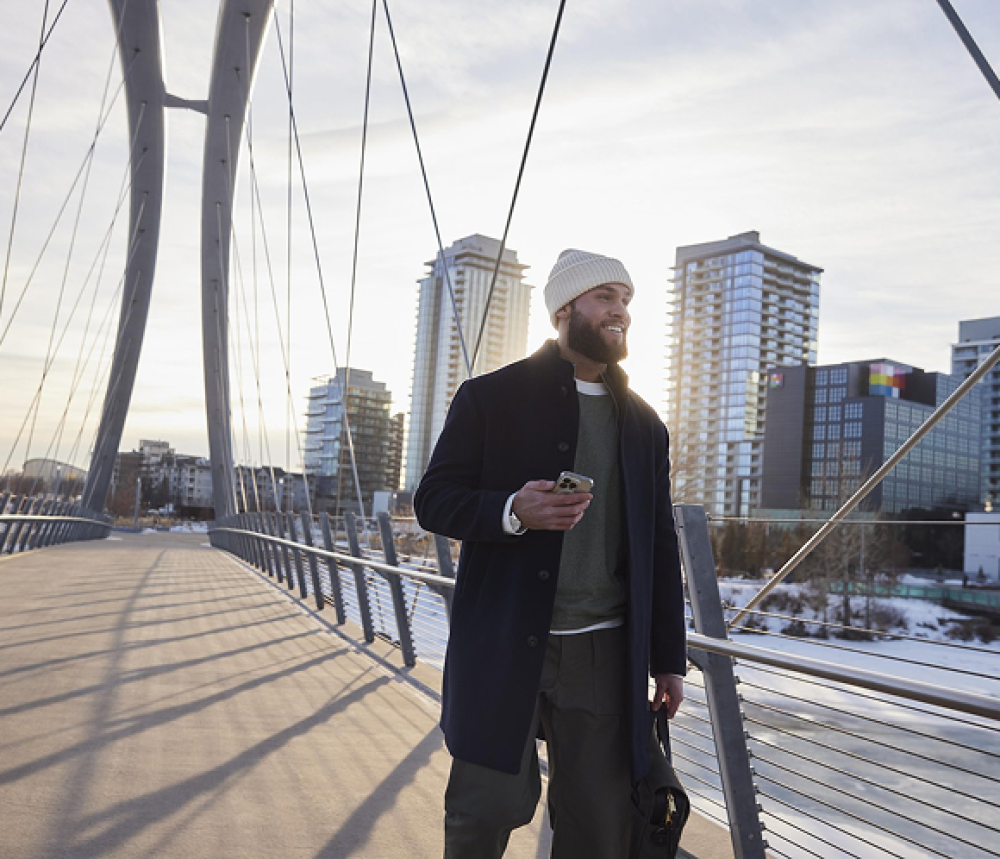 Person walking on suspension bridge with tall buildings in background.
