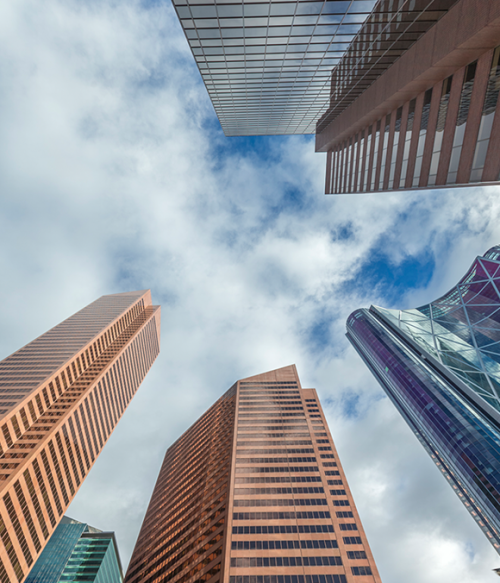 Upward view of tall skyscrapers against cloudy sky.