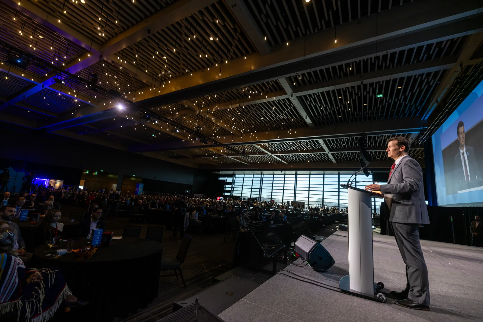 Speaker delivering a keynote address on stage in front of a large audience at a conference venue.