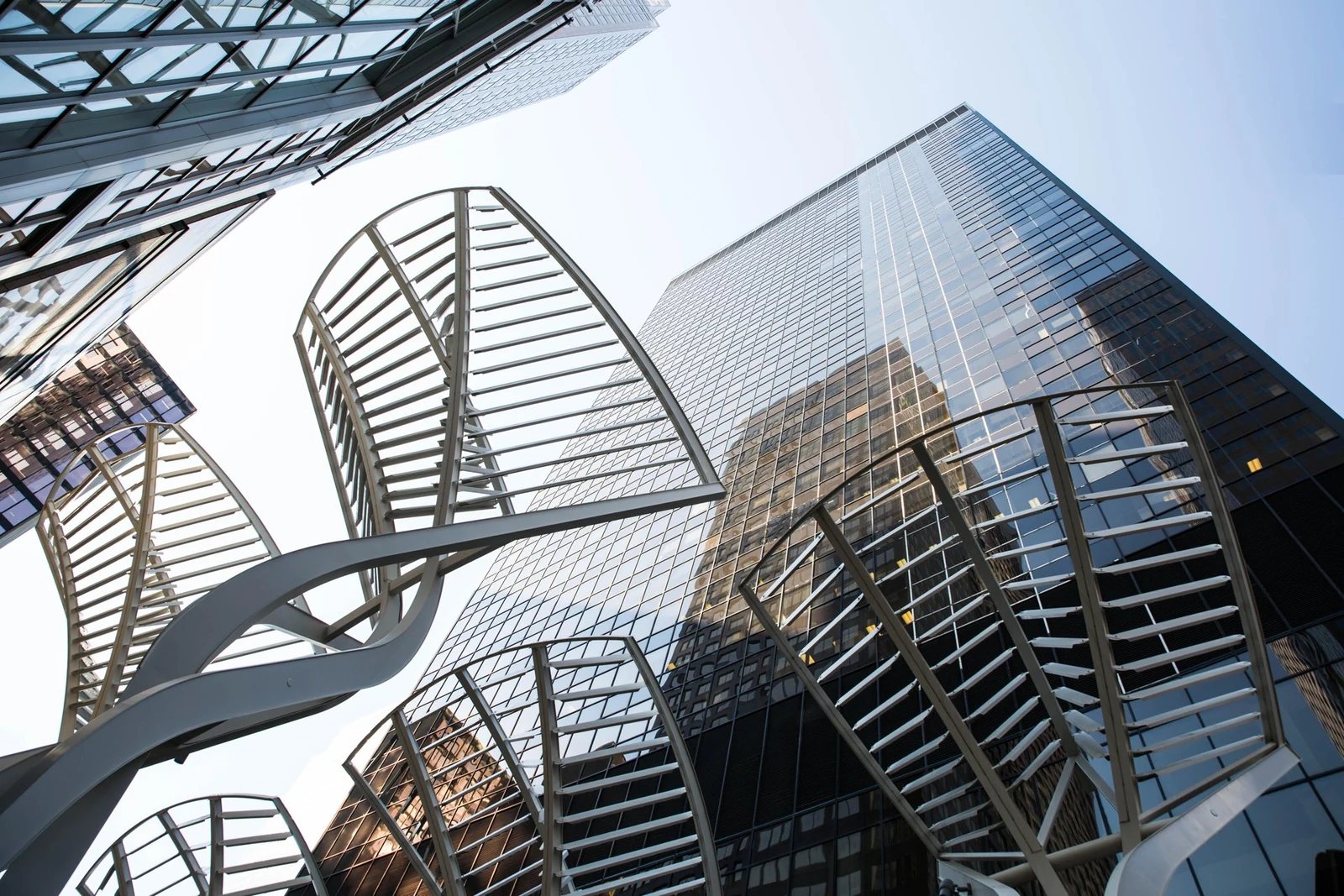 Upward view of modern glass office towers with sculptural metal architectural elements in the foreground.