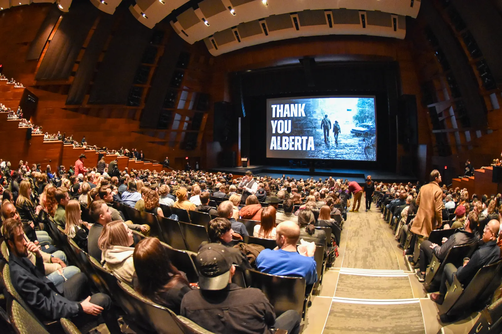 Audience seated in a large theater during a screening with a Thank You Alberta message displayed on the screen.
