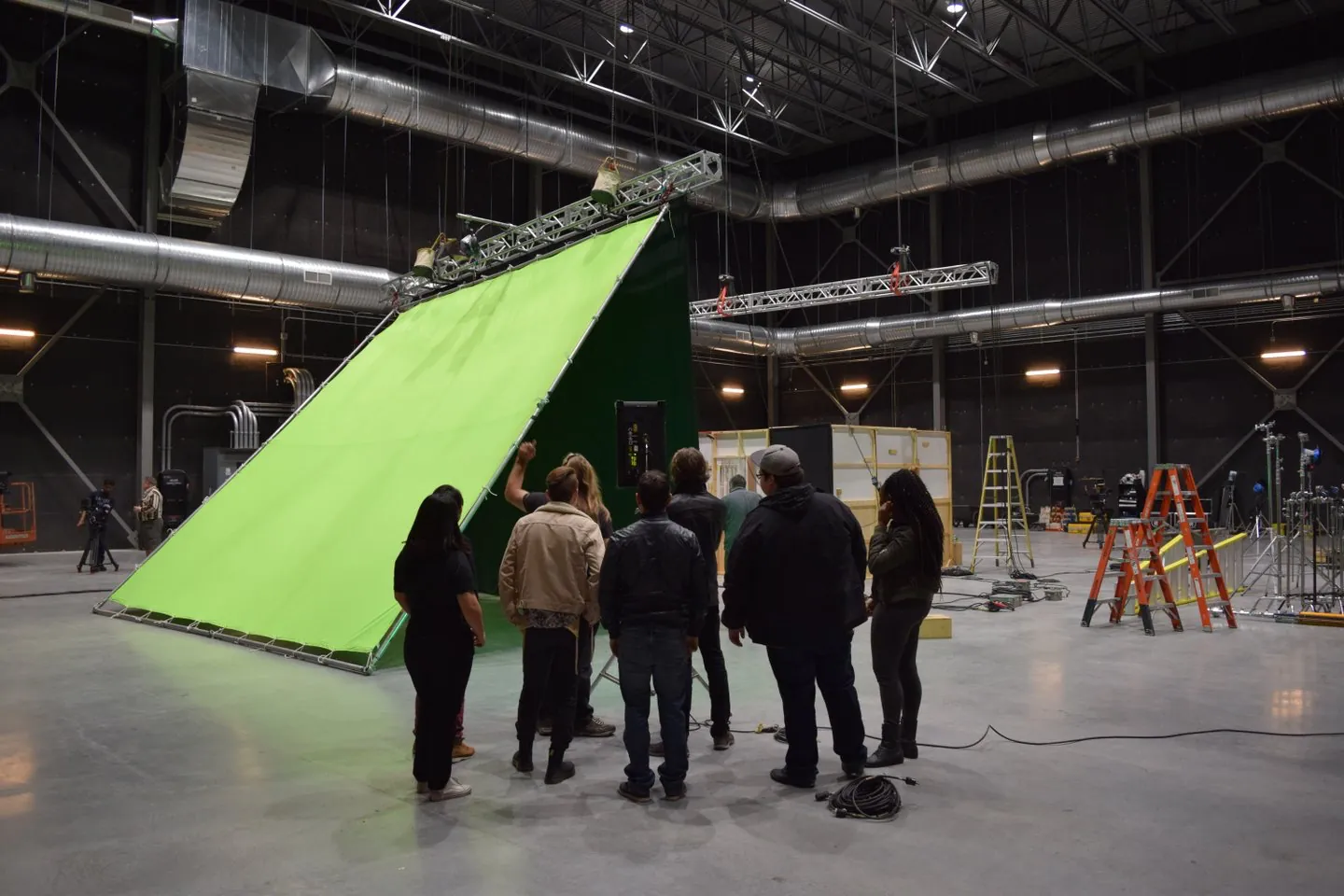 Group of people standing in a large studio around a giant angled green screen stage setup.